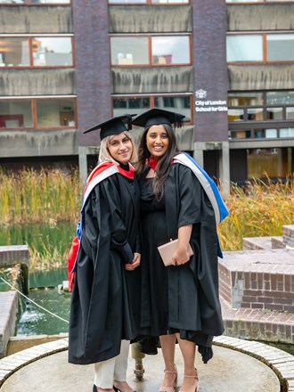 Two smiling female graduations outside at the Barbican centre